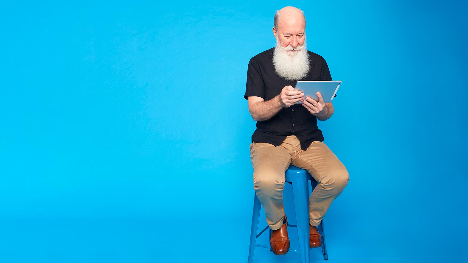 Man sitting on stool using a tablet.