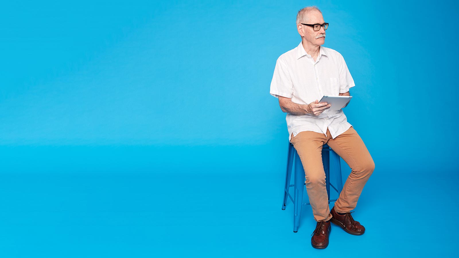 Man sitting on stool using tablet.
