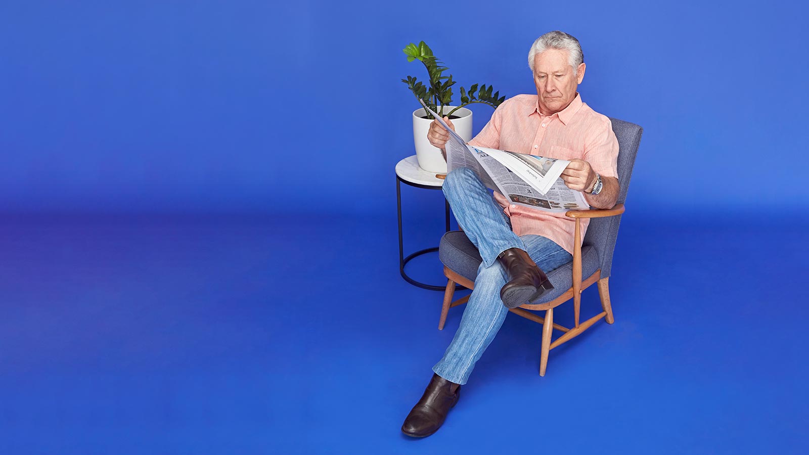 Man reclined in chair, reading newspaper.